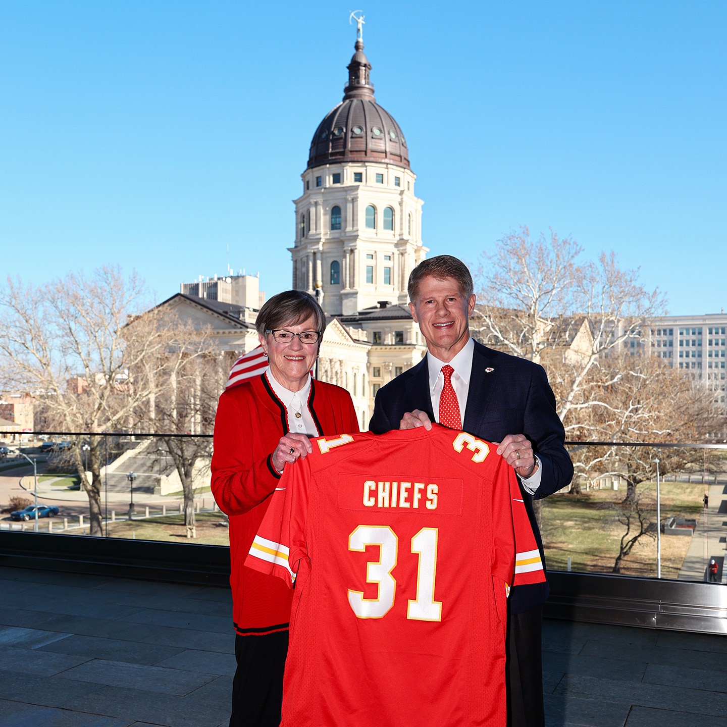 Kansas Governor Laura Kelly and Kansas City Chiefs Chairman & CEO Clark Hunt hold up a Chiefs jersey with the number 31 on it symbolizing the year the Chiefs new stadium is set to open